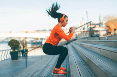 Eine Frau in Sportkleidung und Kopfhörern macht konzentriert ein Treppen-Workout im Freien, um Kondition aufzubauen, mit Blick auf einen Fluss und eine Brücke.
