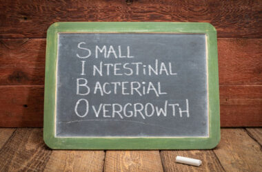 Eine grüne Kreidetafel mit der handschriftlichen Aufschrift Small Intestinal Bacterial Overgrowth (SIBO) in weisser Kreide, daneben ein Stück Kreide auf einer rustikalen Holzoberfläche.