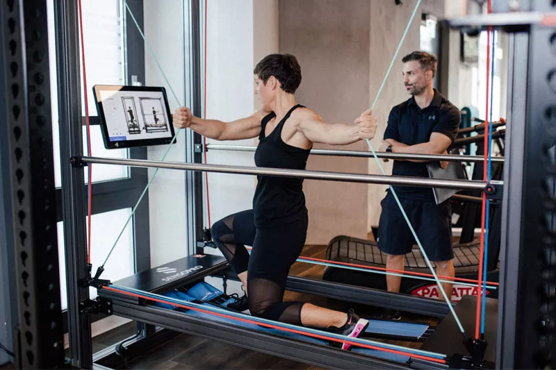 Eine Klientin führt im Personalworkout-Fitnessstudio eine Übung am Sensopro-Gerät aus, während ihr Personal Trainer Marc die Technik überwacht. Diese Übungen eignen sich besonders für Reha-Training oder Training im höheren Alter.
